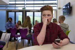 Teenage White Boy holding cellphone at cafeteria table