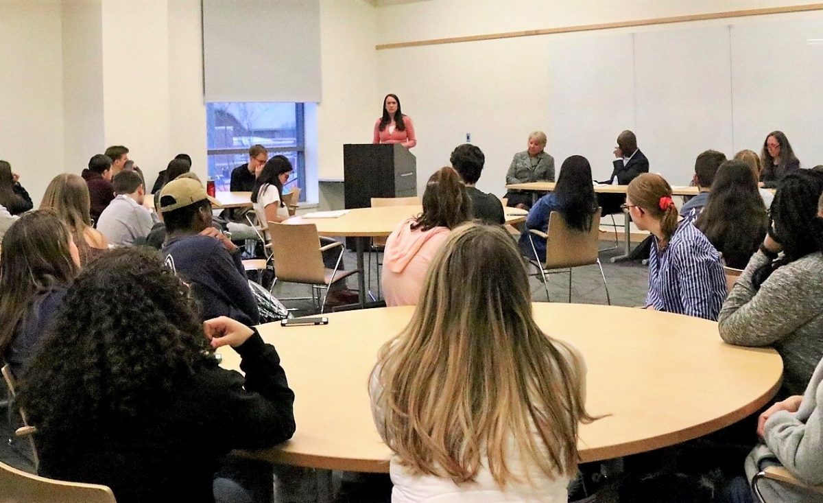 students seated at round tables listen to speaker at podium