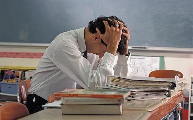 White male teacher at desk with head in hands