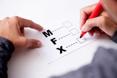 closeup of a young caucasian person about to mark on the X in a form with the letters M for male, F for female and X for the third gender