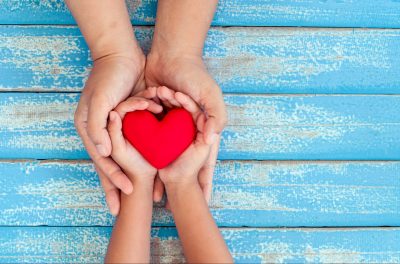 Red heart in child kid and mother hands on old blue wooden table in vintage retro style