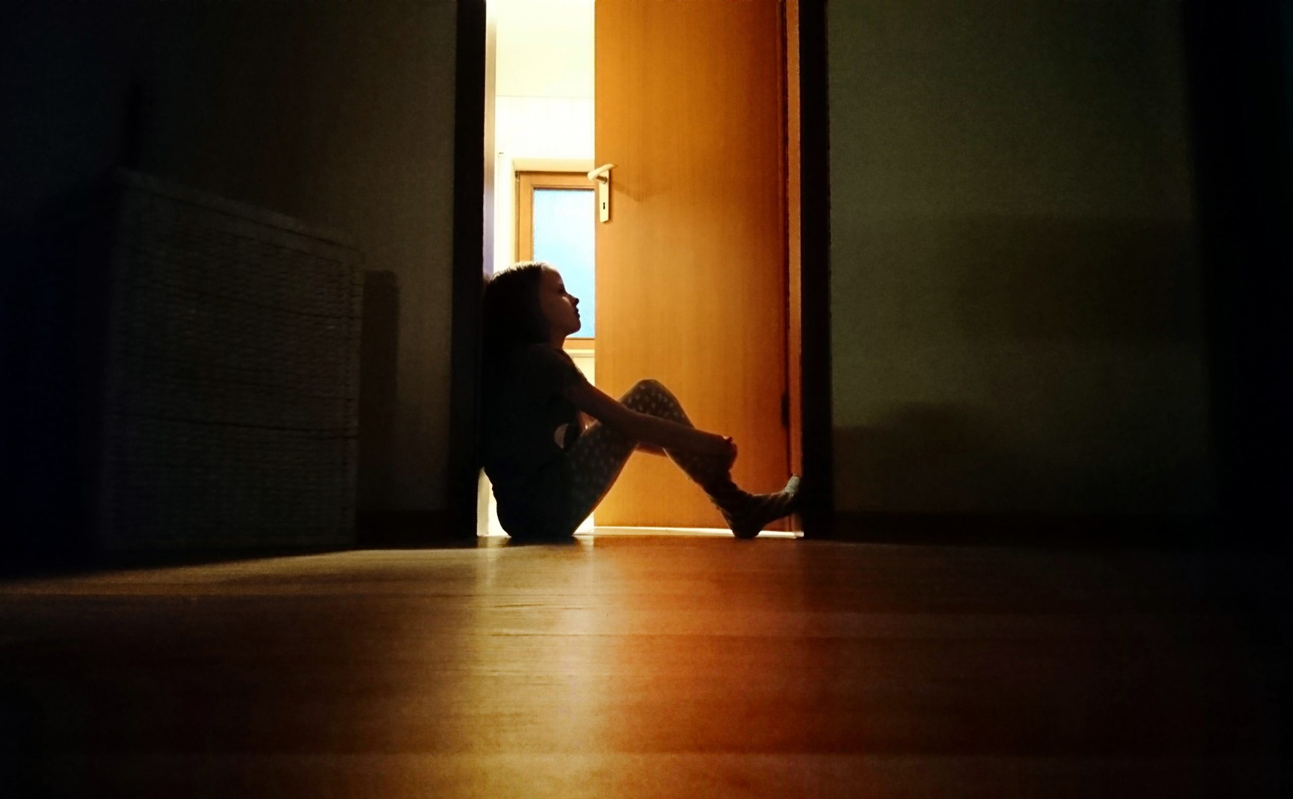 Backlit child sitting in a dark doorway in contemplation