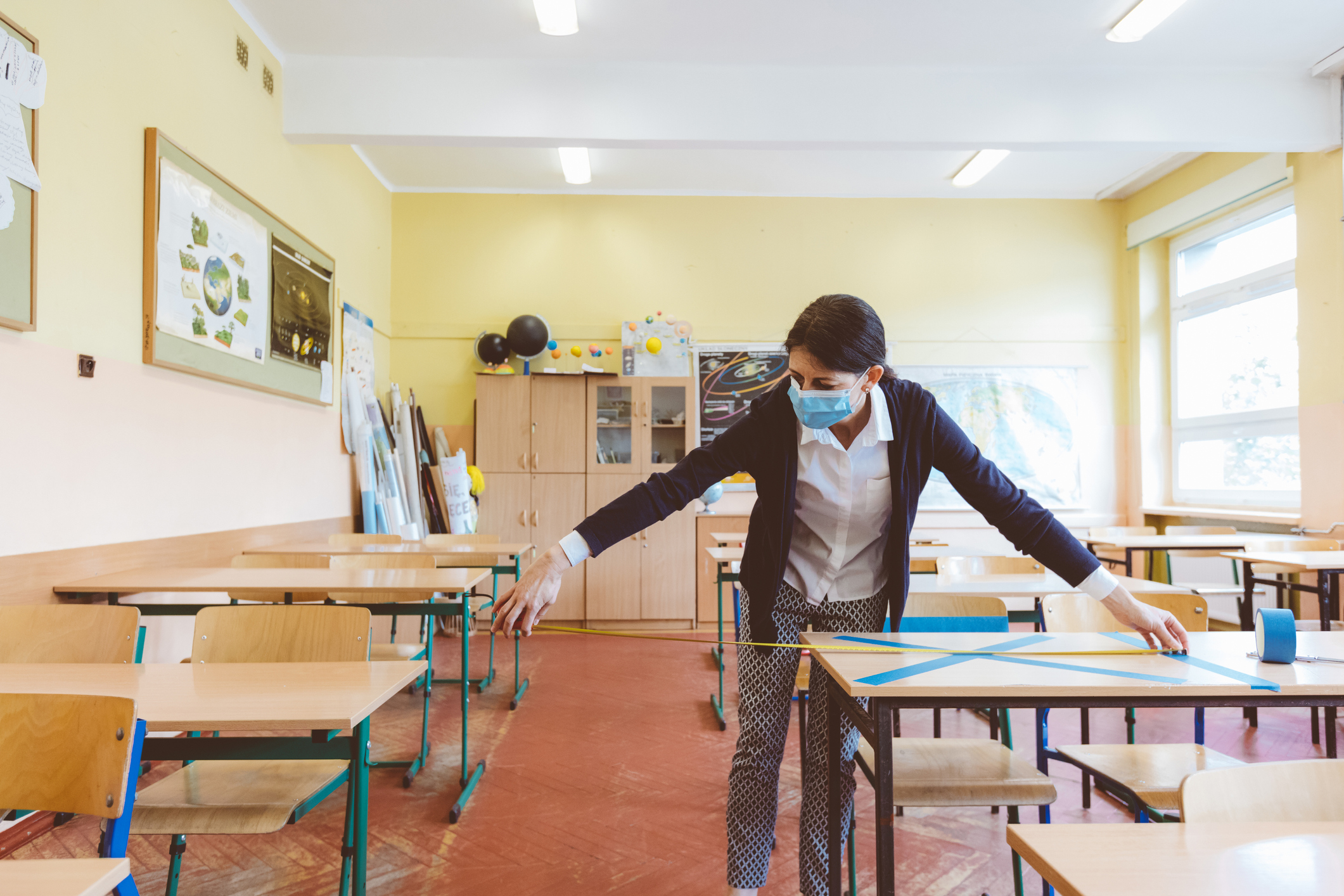 Female teacher measuring and marking places in the classroom that are to be empty after students return to school after the coronovirus pandemic. Covid-19