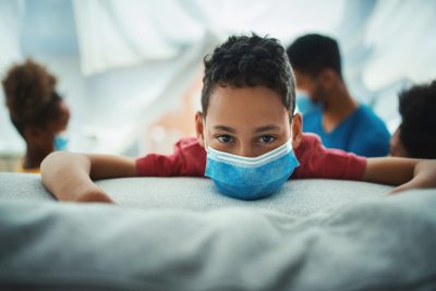 boy wearing mask with head on a couch and family in backgroundronavirus.