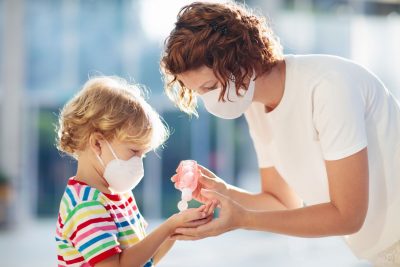 white mother and child with masks; mother is giving boy hand sanitizer during the COVID-19 pandemic