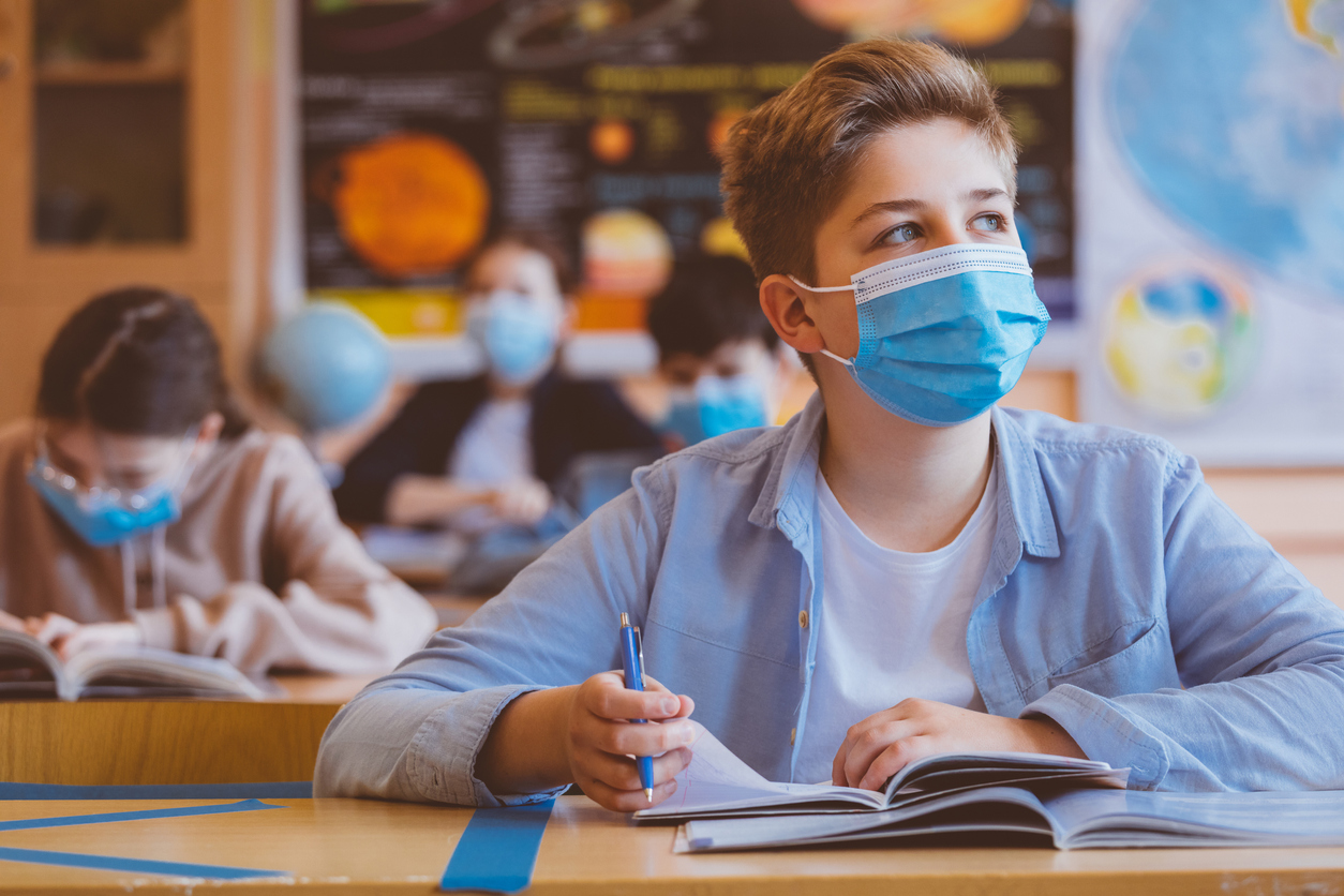 High school students at school, wearing N95 Face masks. Teenage white boy sitting at the school desk, looking away and thinking.