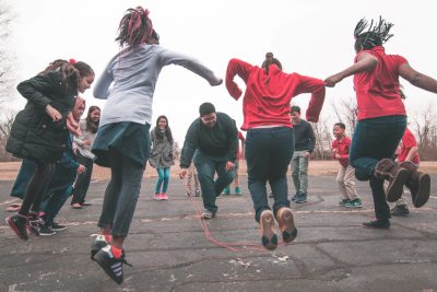 large group of kids playing jumprope or watching on blacktop on outside playground