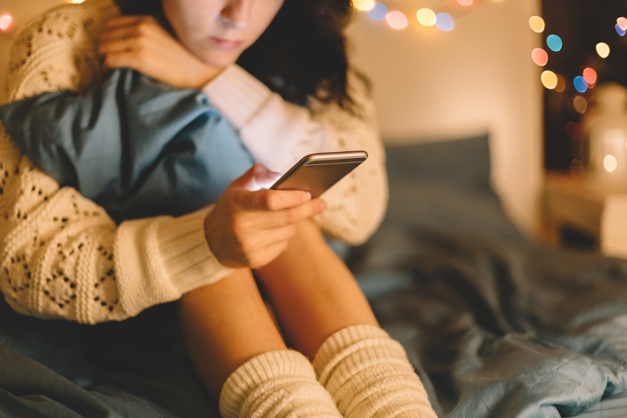 Girl texting on smartphone at home with colorful lights in background