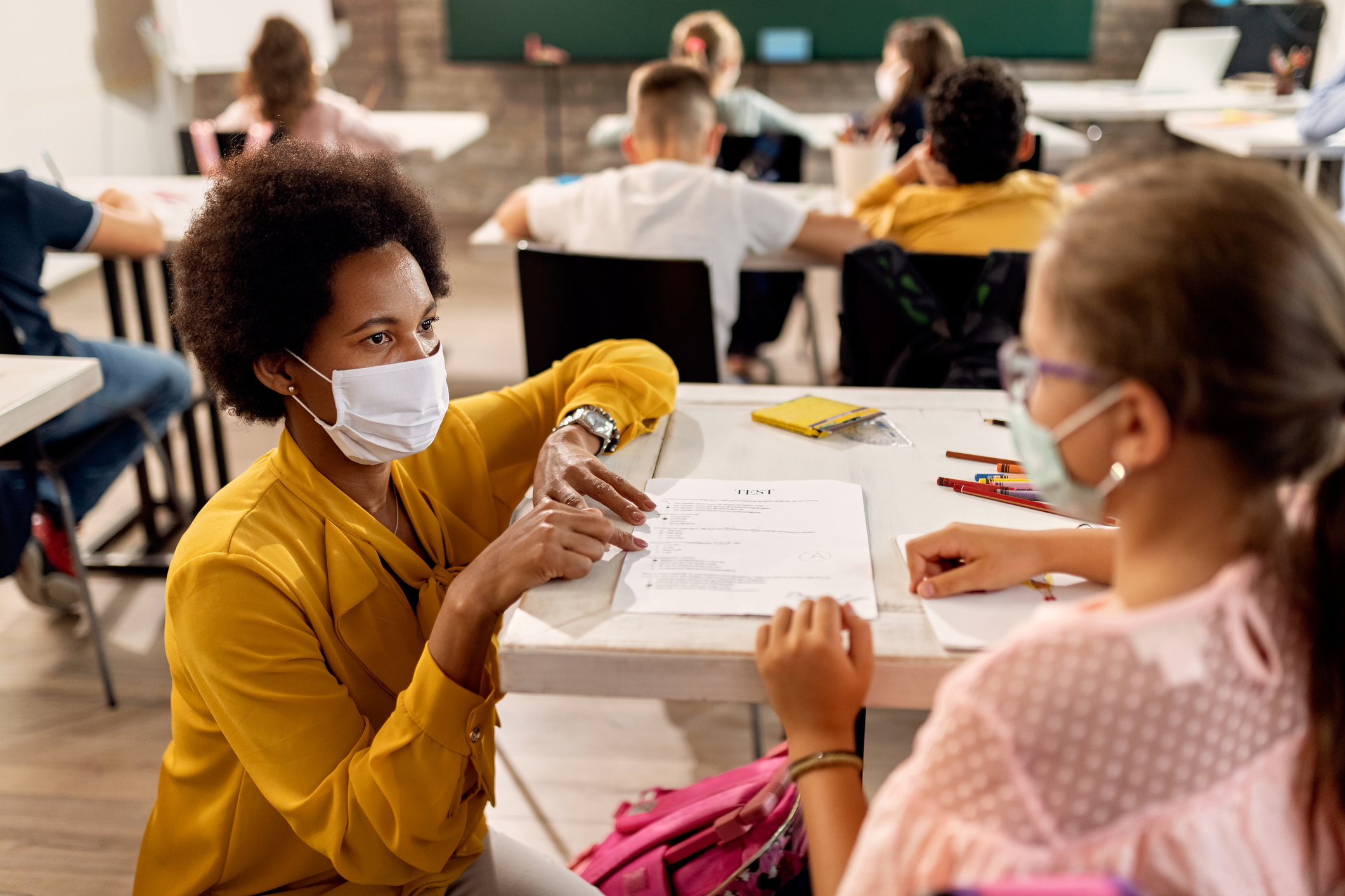 Black teacher with a face mask explaining exam results to elementary student in the classroom