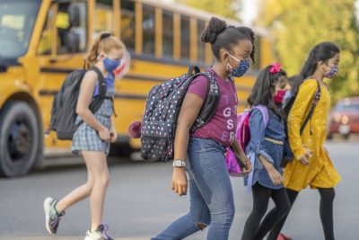 Masked, Multi-racial and ethnic group of students crossing the road after getting off the bus