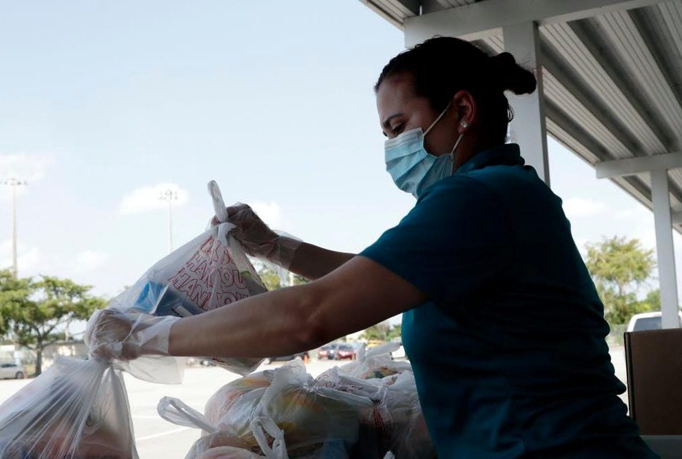 Woman with face mask prepares plastic bags filled with food for distribution