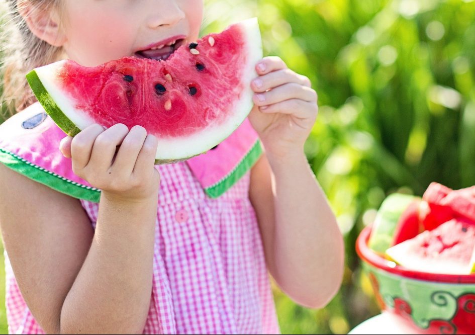 white girl in pink and white checked dress eating watermelon