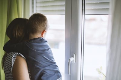 Mom and son looking through window at home. Mom and son embracing.