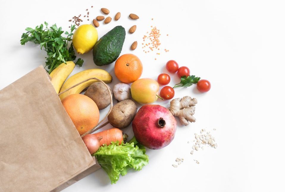 brown paper grocery bag lying on its side with fruits and vegetables spilling out