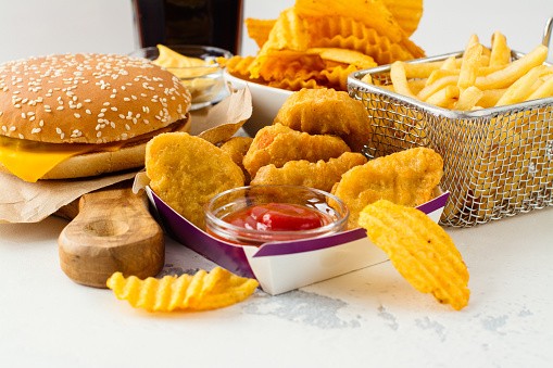 Cheeseburger, chicken nuggets with kethchup, basket of fries and potato chips on a table