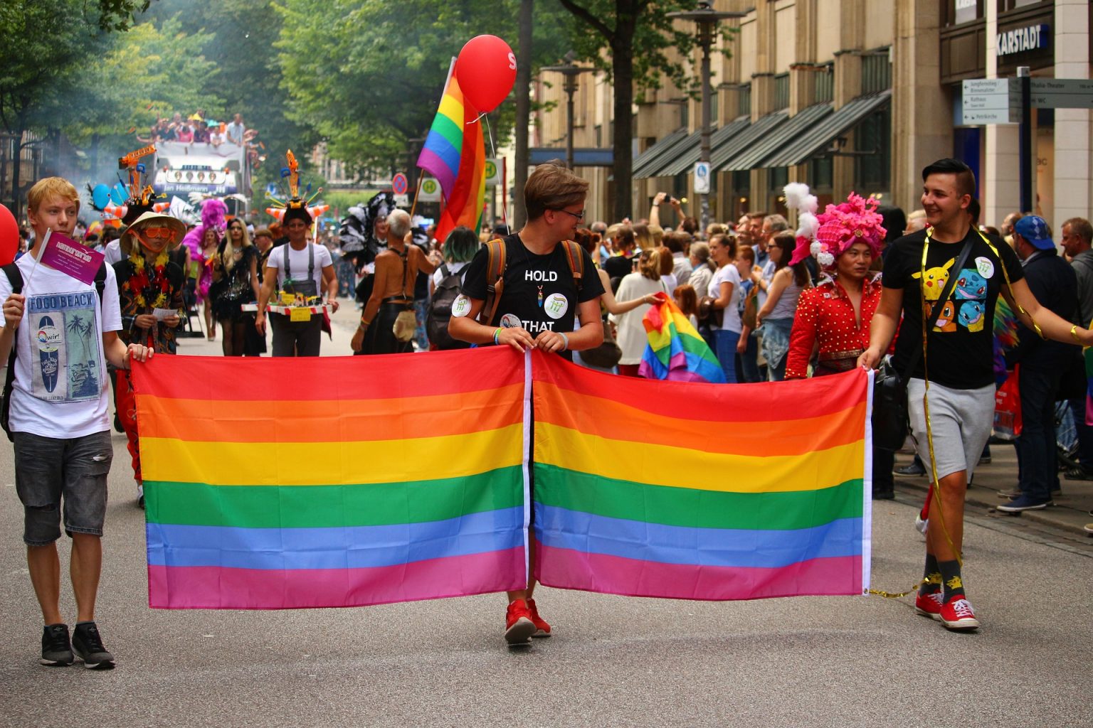 Three young people hold a pride flag in an LGBTQ pride march