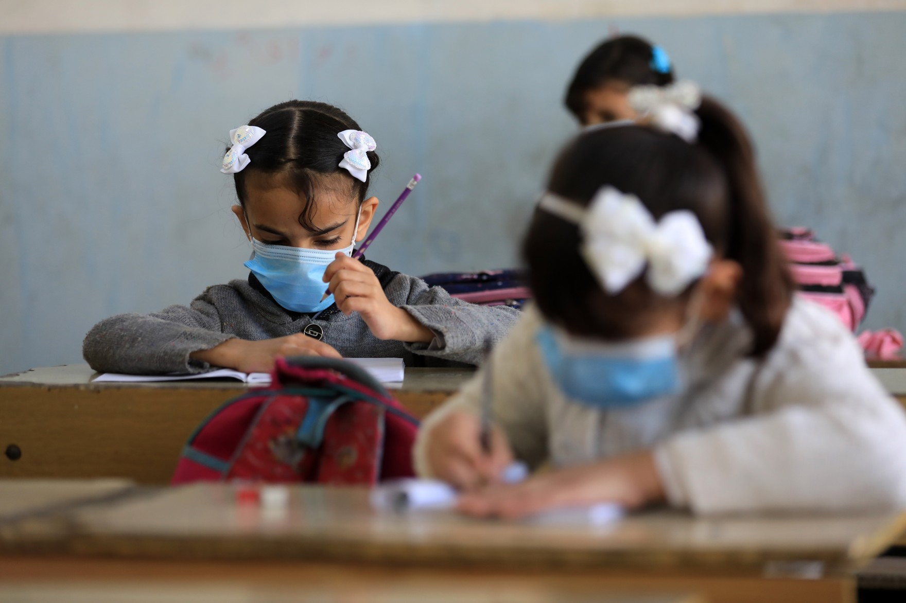  girls sit at desks in classroom with masks