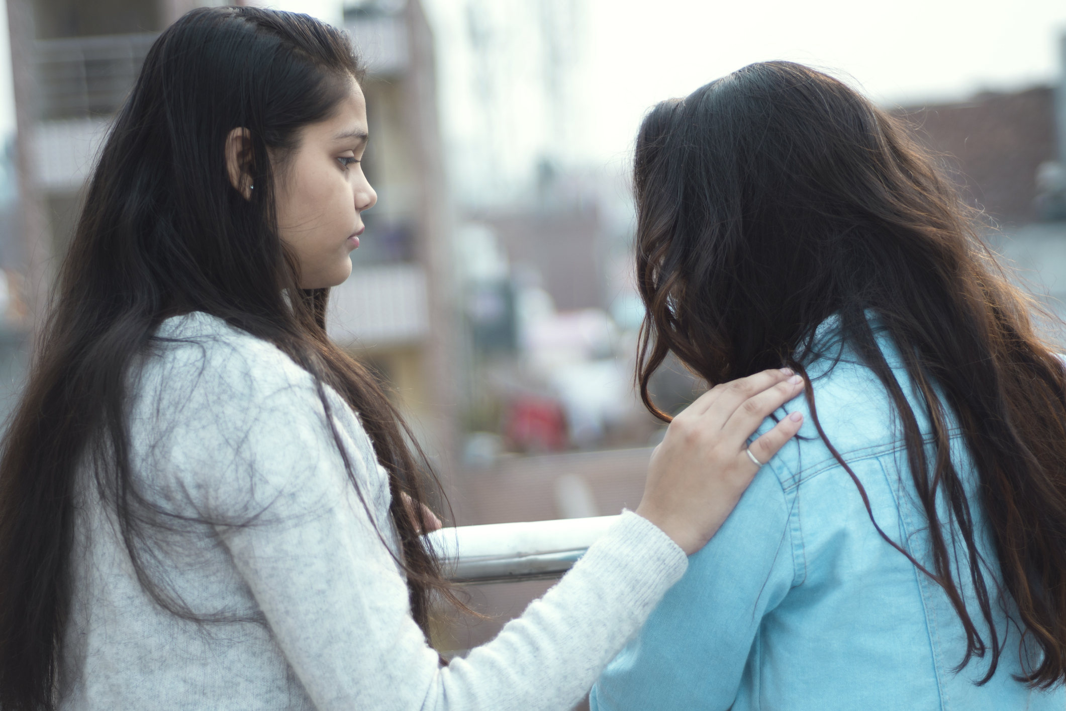 Young woman of color consoling to a depressed friend. outdoor shoot, girls standing in balcony.