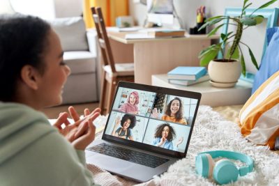 Mixed race teen girl talking with friends on distance video group conference call in bedroom.