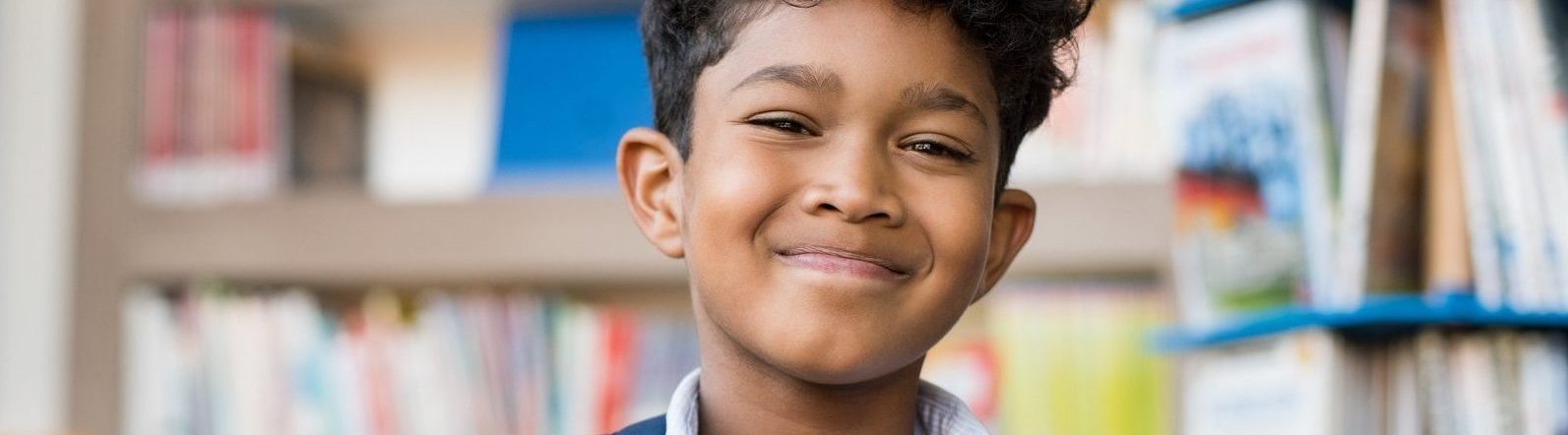smiling Latino or Middle Eastern young boy in front of books