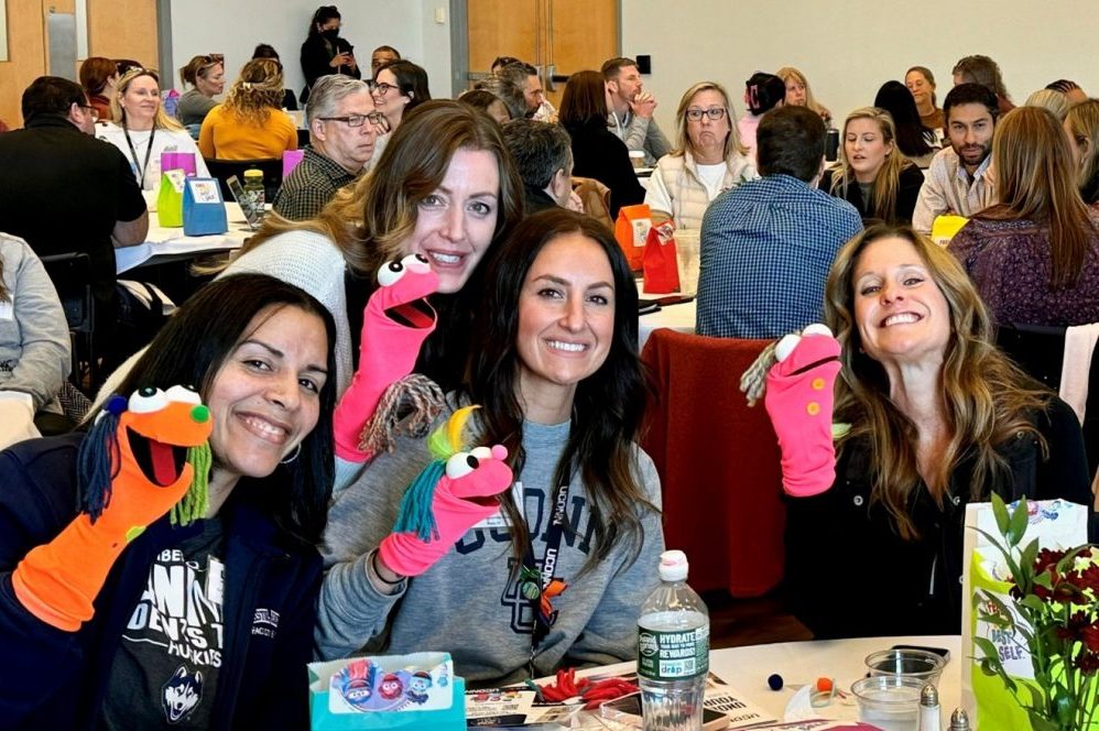 Four female Connecticut School Counselors hold sock puppets and smile at camera