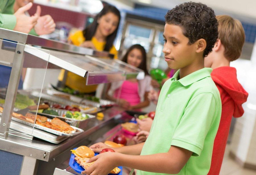 A middle school boy stands in the cafeteria line holding a blue tray