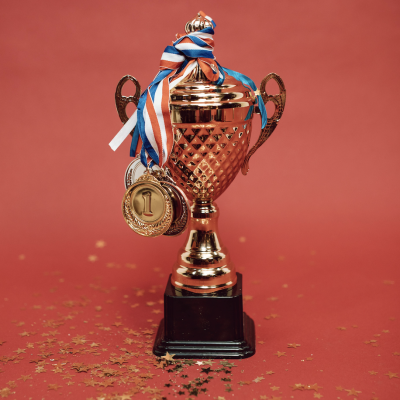 Gold trophy with ribbons and a '1' medal on a red background, surrounded by gold star confetti.