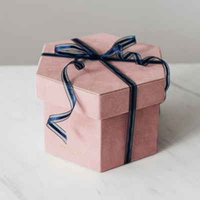 Pink hexagonal gift box with a blue bow on a white marble surface.