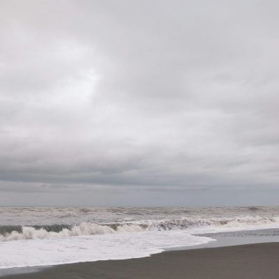 A cloudy day at a beach with waves crashing onto the shore. The sky is overcast with thick clouds.