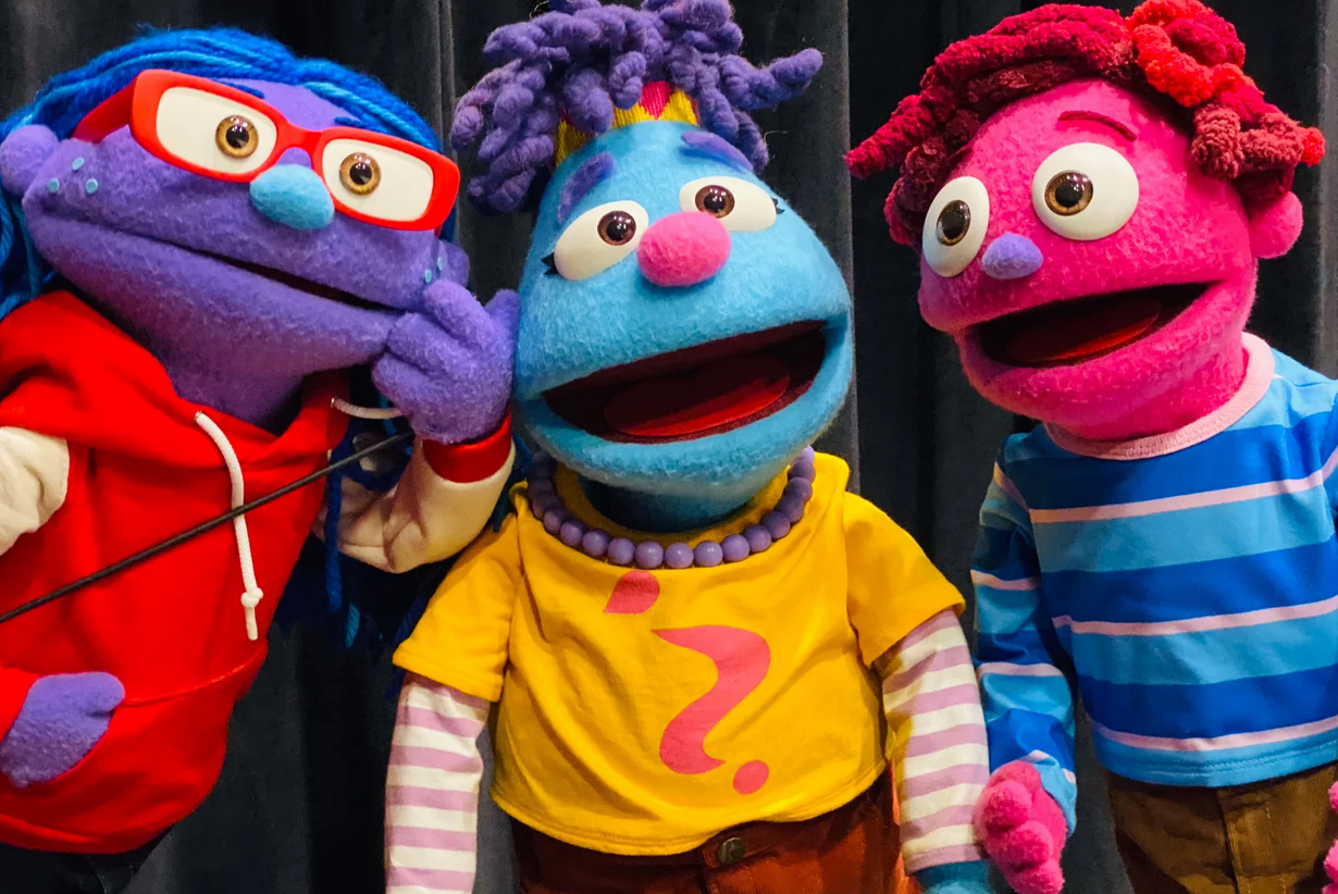 The puppets Mena, CJ, and Nico stand with looks of surprise