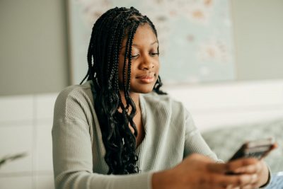 Black female teen wearing grey shirt looks at a phone in her hand with small smile