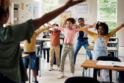 group of kids in classroom facing teacher with their hands outstretched as part of physical activity