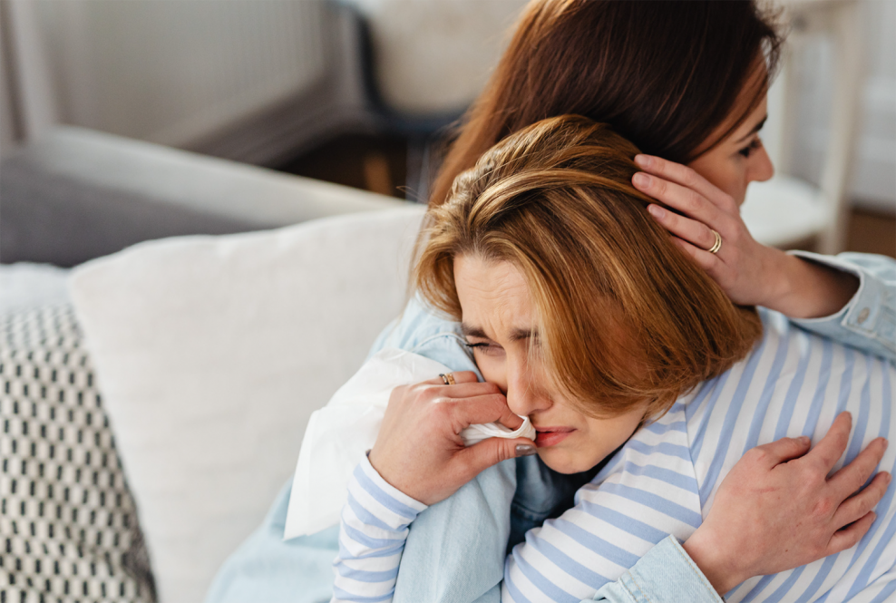 Two women hug. The younger women is crying on the other's shoulder.