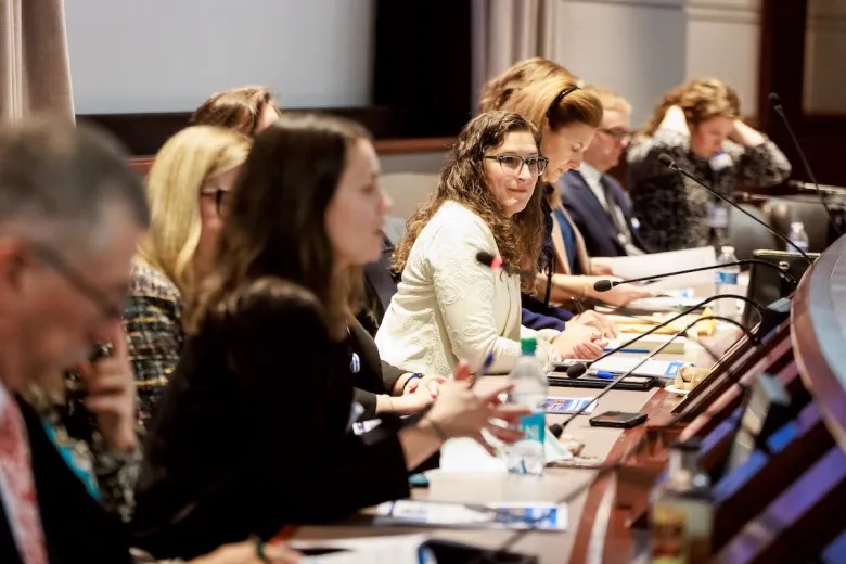 Connecticut State Rep. Jaime Foster smiles in front of a microphone among a row of people in the Connecticut legislative office building