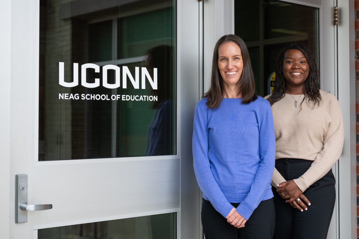 Drs. Jess Koslouski and Mallory Perry stand outside a door that says UConn Neag School of Education