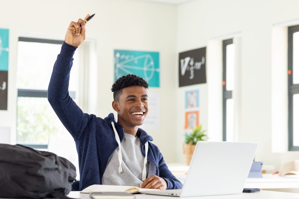 Smiling Black adolescent male raising his hand in class
